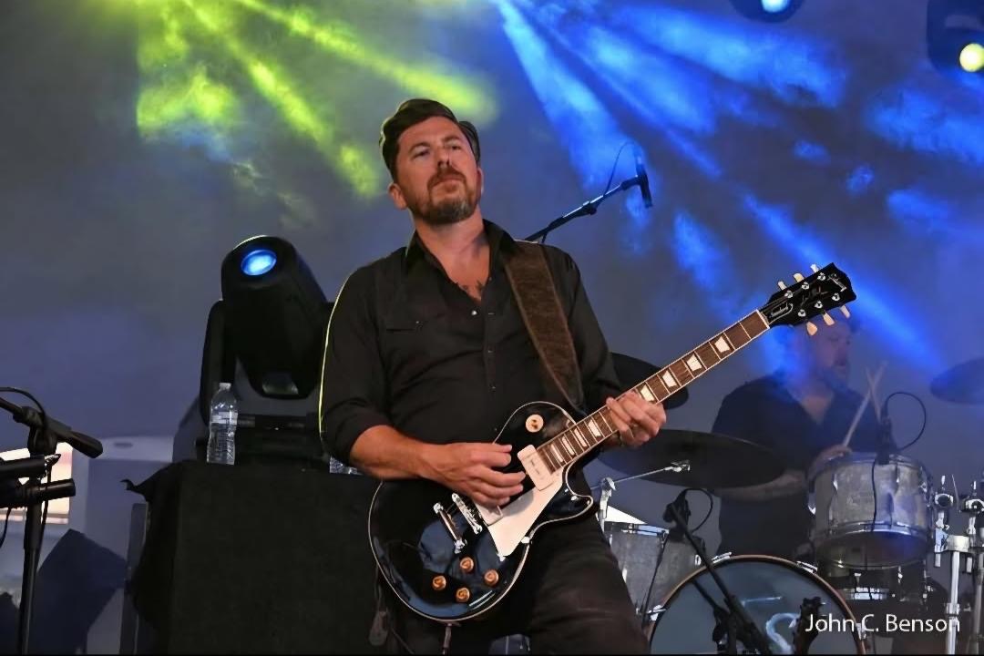 Alex playing electric guitar on stage; photo by John C. Benson